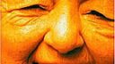 Nahaufnahme einer älteren Person mit orangefarbener Beleuchtung, die lächelt und stolz eine Lücke zeigt, in die ein Zahnersatz passen würde. Der Text Abuela Coca El Ritmo del Barrio steht oben.