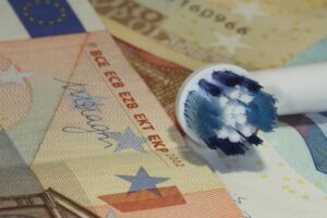 Ein Zahnbürstenkopf mit blauen und weißen Borsten liegt auf verschiedenen Euro-Banknoten.
